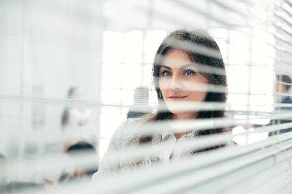 Woman seen through office blinds, suggesting a careful comparison of IFA and RIA wealth management standards.